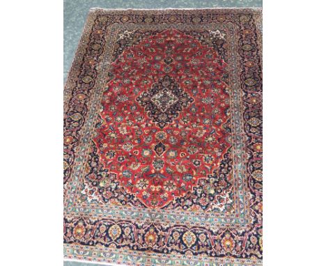 PERSIAN HAND KNOTTED WOOL CARPET, with a central lozenge of floral designs, surrounded by floral motifs on red, surrounded by