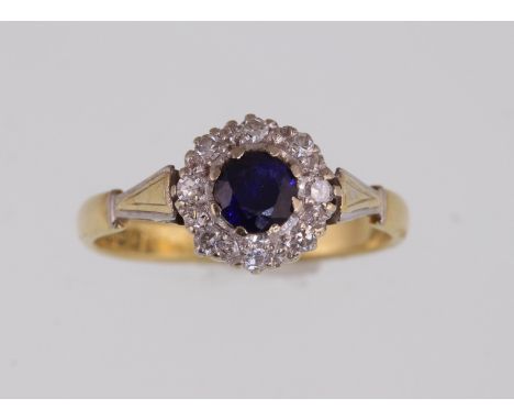 An 18ct H/M sapphire & diamond cluster ring, the round central sapphire surrounded by round brilliant cut diamonds, approx we