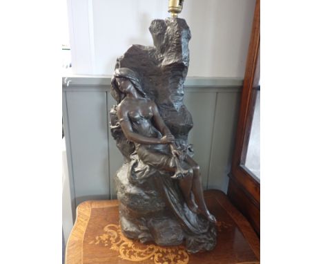 A BRONZED SPELTER FIGURE OF A SEMI-CLAD WOMAN seated on rocks, holding a lily, fitted as a lamp 50 cm high, plus fitting