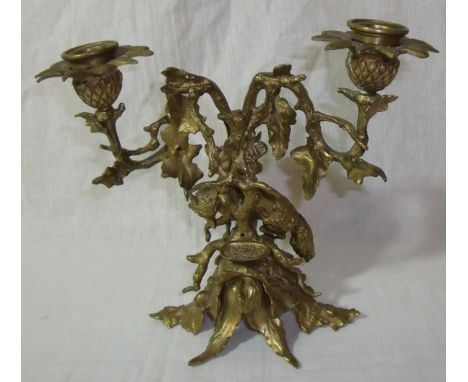 Ornate brass twin candlestick in the form of fox among holly branches and leaves (height