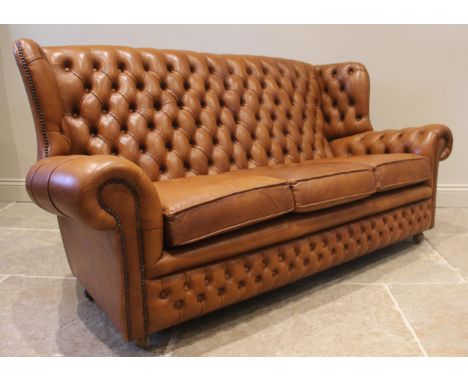 A tan leather wing back sofa and conforming armchair, both with a button back extending to shaped wing backs and scrolled arm