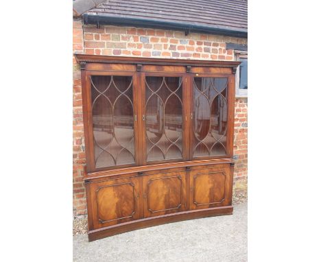 A figured mahogany concave bookcase of Georgian design enclosed three Gothic glazed panel doors over cupboards, on bracket fe