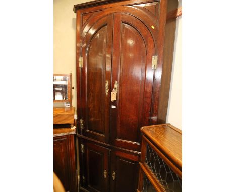A Georgian oak corner cupboard the upper section with shaped shelves enclosed two arch top panel doors, over two doors, on br
