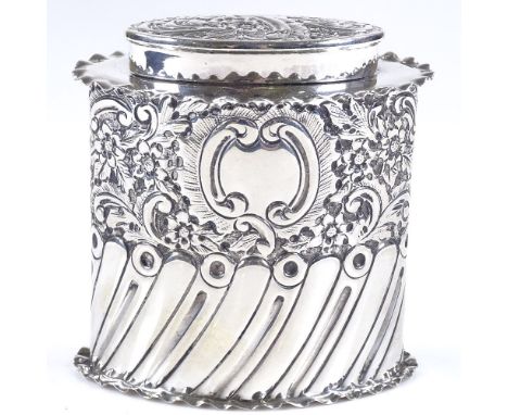 A late Victorian oval silver tea caddy, of half-fluted form with relief embossed floral and scrollwork decoration, with frill