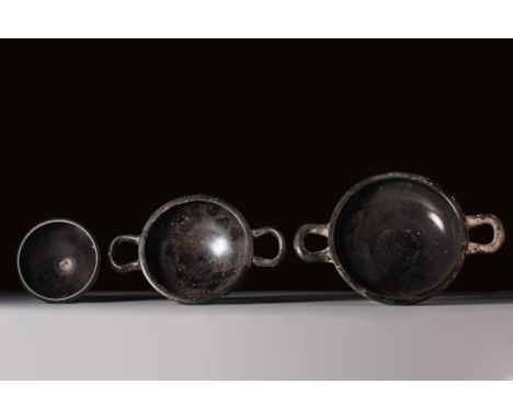 ca. 400 - 300 BC. A collection of three black-glazed vessels. The one on the left is a cup with a hemispherical body set on a