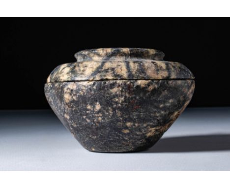 Ca. 3000 - 1790 BC. A kohl vessel carved from breccia, with a tapering lower body and a wide, flattened upper section that fu