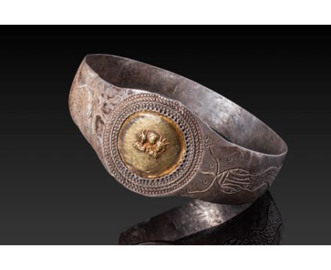Ca. AD 1 - 300. A silver bracelet with a central gold medallion framed by a braided border and decorated in relief with a tri