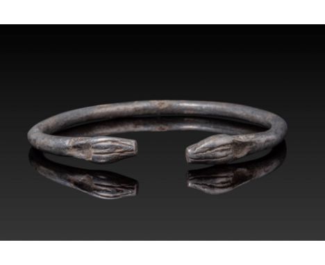 Ca. 600 - 400 BC. A silver bracelet formed from a rounded band with tapering terminals shaped as confronting animal heads, ea
