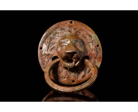 Ca. AD 1 - 200. A bronze door fitting in the form of a lion’s head. The round backplate is cast in high relief with a detaile
