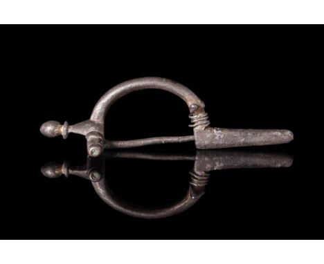 Ca. AD 400 - 600. A silver fibula with an arched bow of round section and a knob finial at the head. The catch plate is cylin