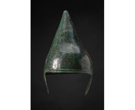 Ca. 800 - 600 BC. A bronze helmet of conical form composed of two vertical halves joined along a central seam reinforced by r