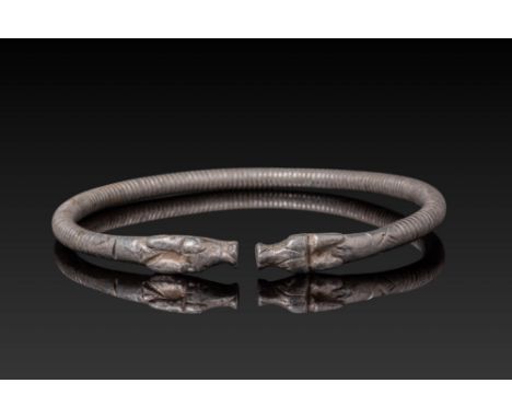 Ca. 600 - 400 BC. A silver bracelet formed from a rounded band with a ribbed body and tapering terminals shaped as confrontin