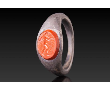 Ca. AD 1 - 200.A red stone intaglio engraved with a standing winged Cupid playing a flute. The oval gem is set in a plain bez