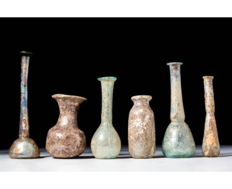 Ca. AD 1 - 300. A collection of six glass unguentaria. The first on the left has a long neck and domed lower body, covered in
