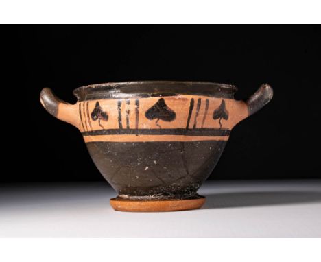Ca. 500 BC. A black glaze skyphos with a deep, tapering body, upturned handles, and a ring base. The upper section is decorat
