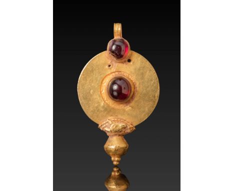 Ca. 300 - 100 BC. A gold pendant composed of a flat-section, circular medallion with two mounted garnet cabochons, one centra