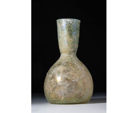 Ca. AD 300. A translucent pale green glass unguentarium with a domed body tapering into a tall flaring neck with a circular o