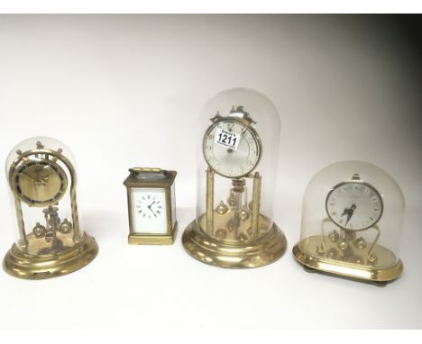 A brass cased carriage clock and three brass anniversary clocks under a glass dome. (4)
