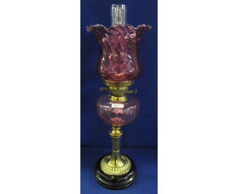 Early 20th Century brass double burner oil lamp with cranberry glass wrythen reservoir on brass pedestal with ceramic base.  