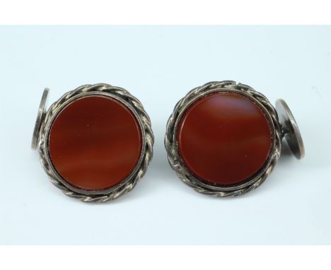 A pair of early 20th Century carnelian  and white metal cufflinks, having 16 mm diameter hardstone panels in a rope twist bez