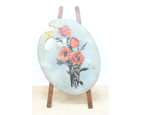 A fire screen in the form of an artist's pallet, on an easel type stand, the front painted with a floral still life, 20th Cen
