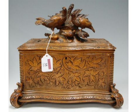 A late 19th century Black Forest carved tea caddy, of serpentine outline,the hinged cover surmounted with game birds, the who