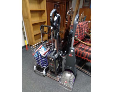 A Shark vacuum together with a Bissel carpet cleaner and a trolley containing shaver and two books 