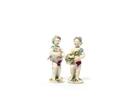 Two Bow figures of putti, c.1758-60, one standing with a puppy, the other with a basket of flowers, each wearing a floral sas