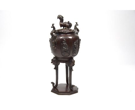 A Japanese bronze koro with domed cover surmounted by a Kirin, the body with kacho-ga relief decorated panels standing on tal