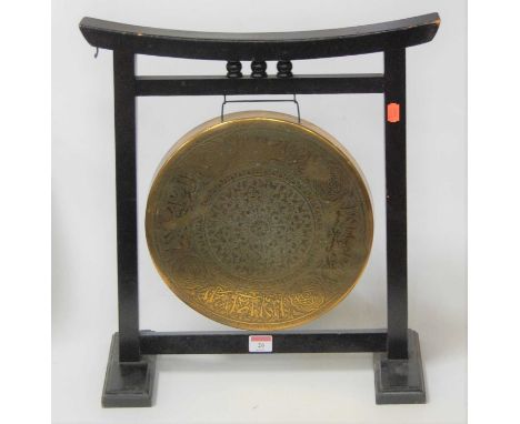 An Eastern embossed brass dinner gong, within an ebonised surround, w.43cmCondition report: Table gong – max w.46cm, h.50cm.L