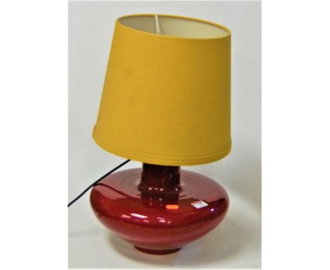 A large red glazed ceramic table lamp of squat circular form with yellow conical shade, height 50cm including shade