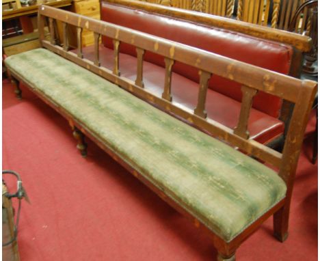 An extremely long late Victorian railway waiting room bench having green upholstered seat and raised on turned supports, leng