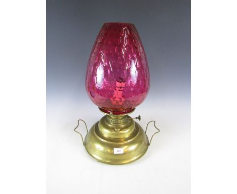 A large brass oil lamp with ruby glass shade