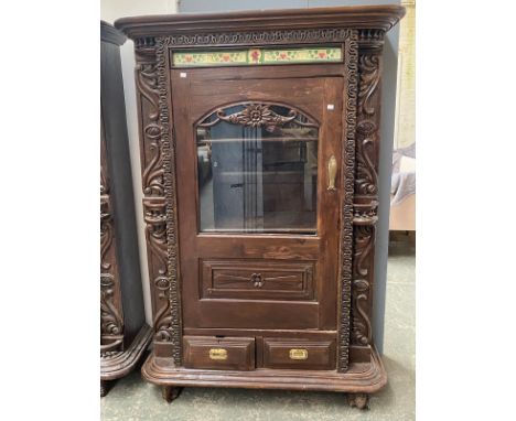 An Indo-Portuguese carved cabinet with Art Novueau tiled frieze over a glazed cupboard door, two doors below, on stylised ele