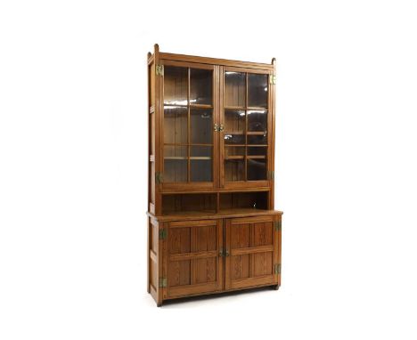A late Victorian pitch pine bookcase cupboard, having twin glazed upper doors with interior shelves, over open compartment to