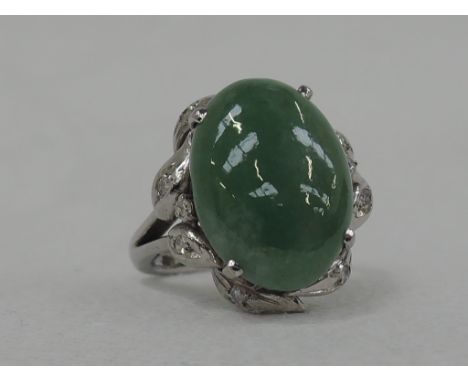 A lady's dress ring having a jade cabouchon in a raised claw mount with diamond set moulded leaf surround on a white metal lo