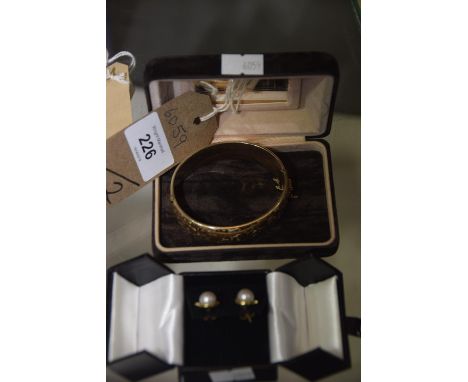 A Gold coloured bangle with chased decoration, and a pair of 9ct gold and pearl earings. (2) 