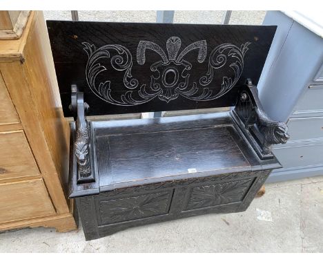 A CARVED OAK MONK'S BENCH WITH LION ARMRESTS AND HINGED UNDER SEAT COMPARTMENT - CONVERTS TO A TABLE 