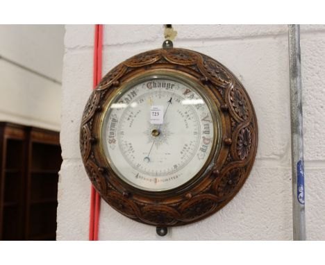 A circular aneroid barometer with carved oak frame.