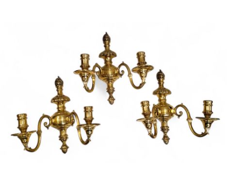 A set of three brass two light wall sconces, reel shaped sconces, leafy finials, 34cm high 