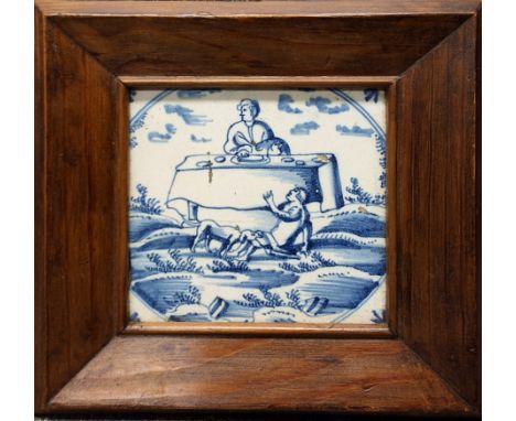 An 18th century Delft tile, decorated in underglaze blue with a person seated at a table, another on the floor with a hound, 