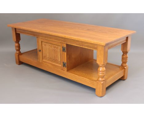 A blonde oak coffee table - the undertier with central cupboard with linenfold carved door. (LWH 122 x 51 x 46.5cm)