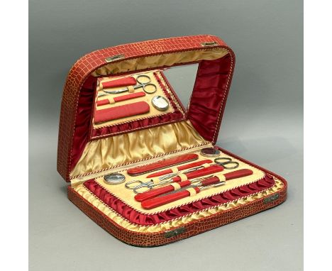 A 1950s ladies vanity case in red mock crocodile - the fitted interior with red and gold ruched lining, mirror and complete c