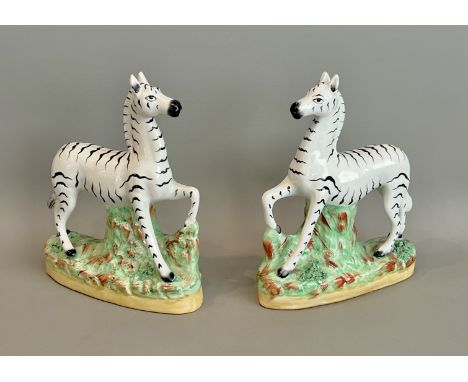 A pair of 19th century Staffordshire figures of zebras - on naturalistic bases, each with one front foot raised, 20.8cm high.