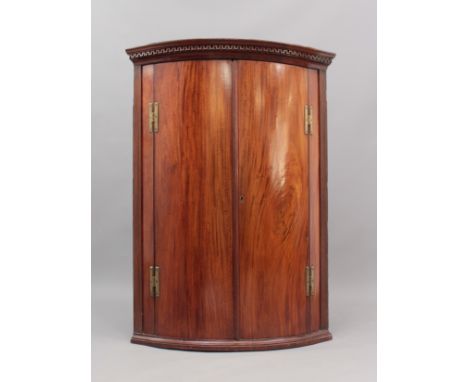 A George III bowfronted mahogany corner cupboard - early 19th century, the key fret cornice over reeded supports, nicely&nbsp