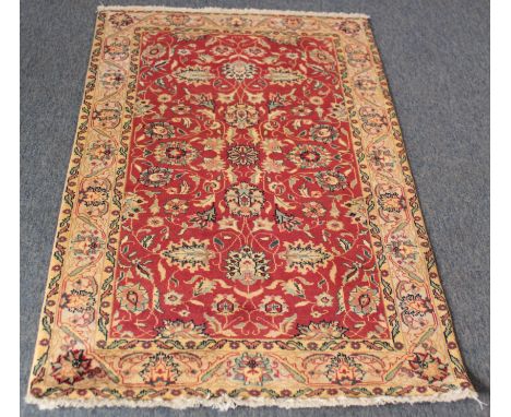 A small hand-knotted wool rug - late 20th century, the madder field with all over floral vine decoration, within an ivory flo