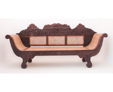 An Anglo-Indian carved hardwood and caned settee - late 19th / early 20th century, the shaped back profusely carved with a ce