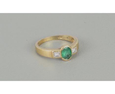 An 18ct yellow gold, emerald and diamond three stone ring - stamped '750', the central 6 x 4.75mm oval cut emerald flanked by