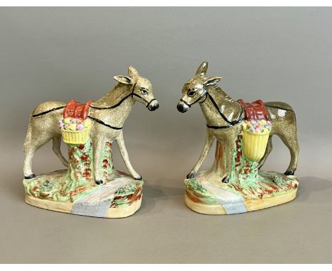 A pair of 19th century Staffordshire figures of donkeys - carrying baskets of fruit across their backs, on naturalistic bases