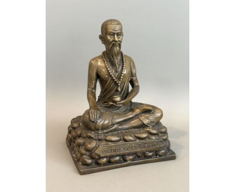 An Oriental bronze figure of Luohan (the emaciated monk) - 20th century, seated on a mat on a stony base, holding a pomegrana